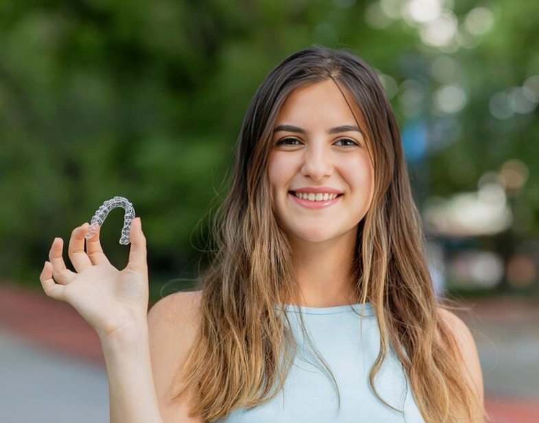 Teen patient holding Invisalign clear aligners at Dr. Bryan Elvebak Orthodontics in Plano, TX.