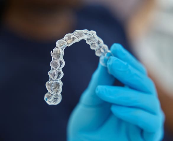 Gloved hand holding clear orthodontic aligner for teeth straightening treatment.