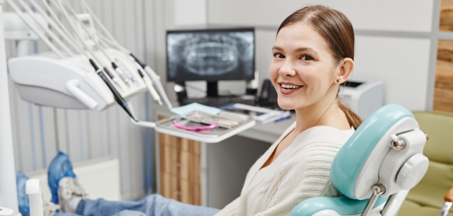 Smiling woman in dental chair at orthodontic office with equipment visible in background.