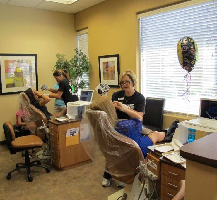 Orthodontic office staff assisting patients in bright yellow waiting room with modern furniture and décor.