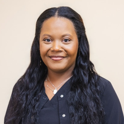 Professional headshot of woman with long black hair smiling at camera in office setting.
