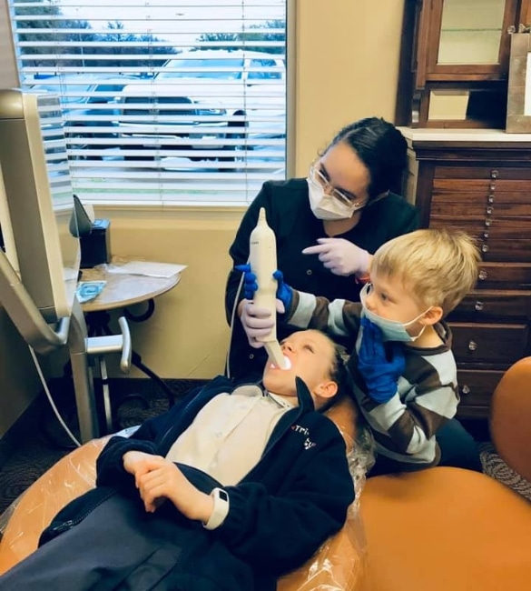 Orthodontist showing young child dental model in bright office treatment room with window.