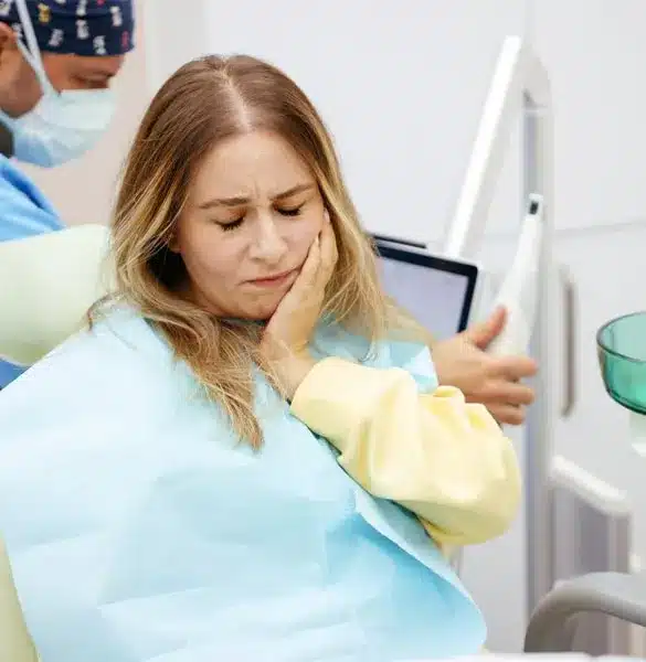 Woman in dental chair holding jaw in pain during emergency dentistry visit