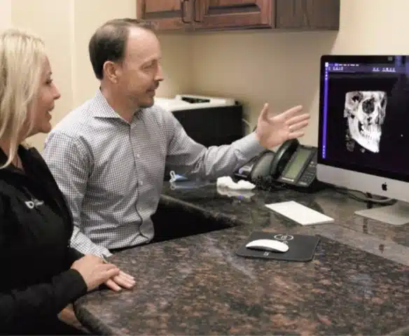 Orthodontist and female staff member reviewing dental X-ray on computer monitor at desk.