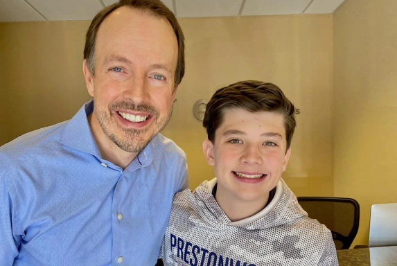 Adult man and young boy smiling together in orthodontics office setting.