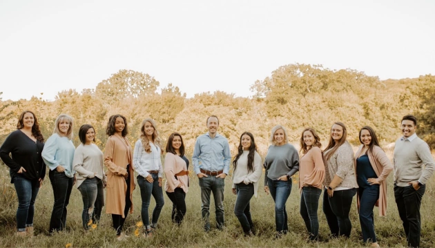 Large group of people standing in a line outdoors in a field with trees.